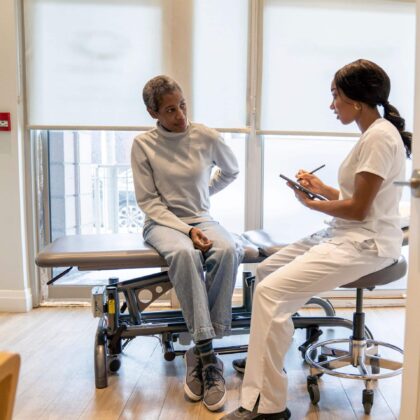 A nurse case manager consulting with a patient sitting on an exam table in a bright medical office.