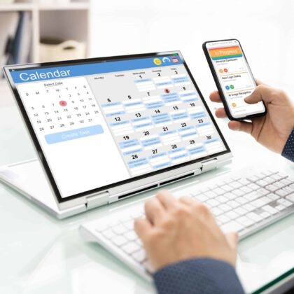 Person using a digital calendar on a laptop and smartphone to schedule and organize tasks in an office setting